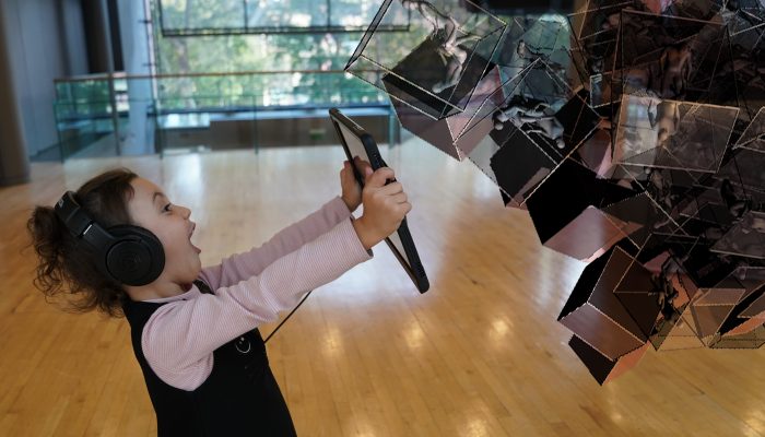 Young girl wears headphones, pointing an iPad at an installation expressing joy