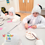 Children dressed in white sitting around table with pens and paper