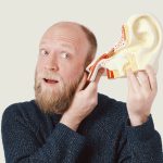 Man pretending to listen through sculpture of ear